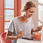 Smiling woman savoring a fresh breakfast with juice and dessert indoors.