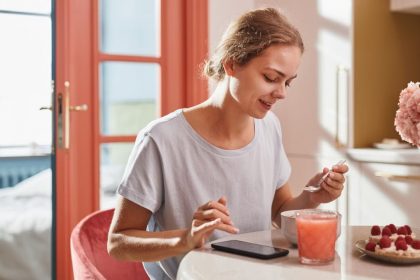 Smiling woman savoring a fresh breakfast with juice and dessert indoors.