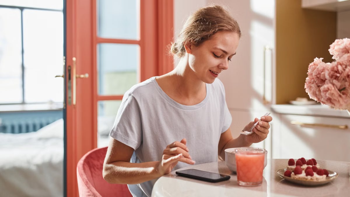 Smiling woman savoring a fresh breakfast with juice and dessert indoors.