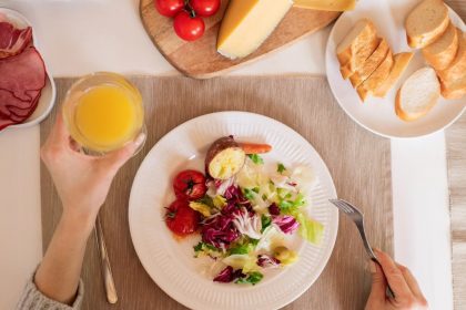 A top-view of a delicious breakfast setting featuring a salad, bread, cheese, tomatoes, and orange juice.
